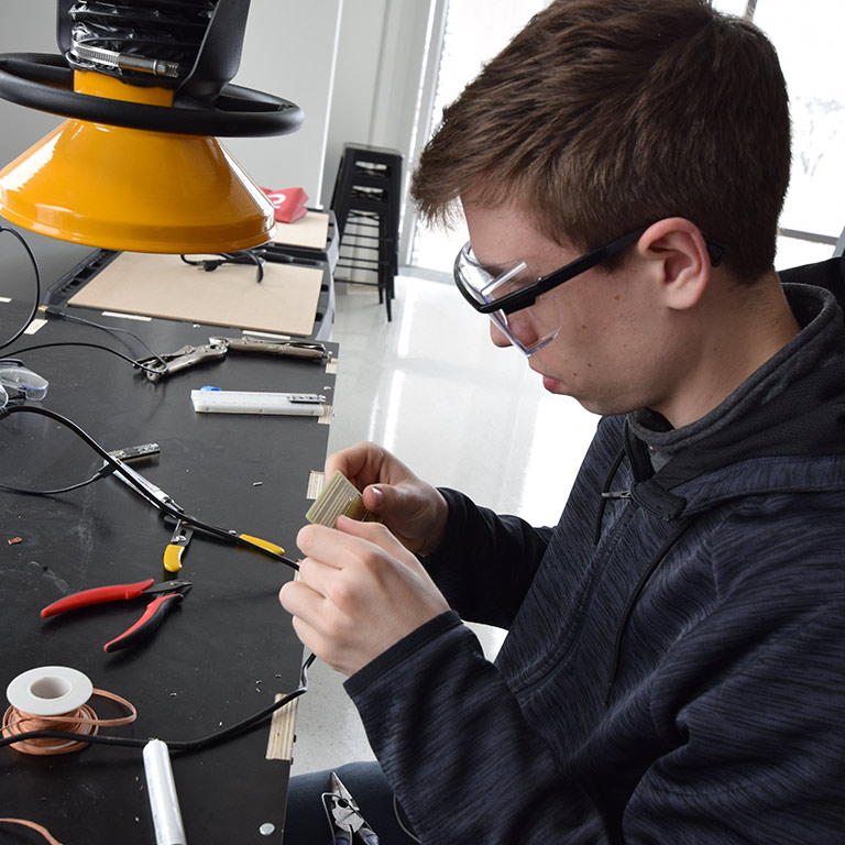 A student wears goggles while he works on a circuit board in a makerspace in Luddy Hall.